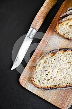 Traditional French country bread slices and pocket knife on a cutting board