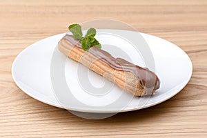Traditional french dessert. Delicious eclair with custard and chocolate icing on a white plate with mint leaf.