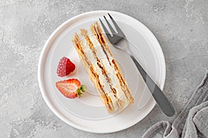 Traditional French dessert millefeuille with vanilla cream and fresh berries on a white plate on a gray concrete background