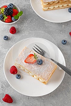 Traditional French dessert millefeuille with vanilla cream and fresh berries on a white plate on a gray concrete background