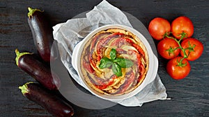 Traditional French dish quiche with eggplants and tomatoes in the baking dish decorated with fresh basil leaves. Vegetable tart