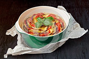 Traditional French dish quiche with eggplants and tomatoes in the green baking dish decorated with fresh basil leaves