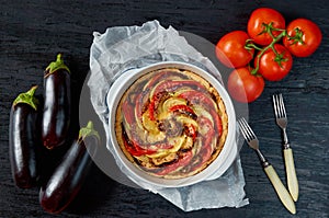 Traditional French dish quiche - pie with eggplants and tomatoes in the baking dish. Homemade vegetable tart on the black table