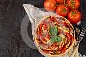 Traditional French dish quiche with vegetables and cheese on black background. Vegetarian eggplant tart decorated with tomatoes