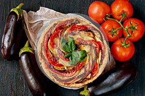 Traditional French dish quiche with vegetables and cheese on the black background. Vegetarian tart decorated with fresh eggplants