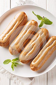 Traditional french eclairs filled with coffee cream and topped with soft Buttery Homemade Caramels close-up in a plate. Vertical