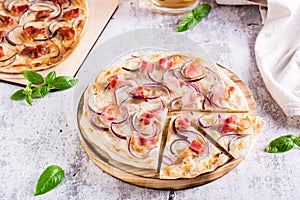 Traditional french flambee tart with cream cheese, bacon and onion on a board on the table