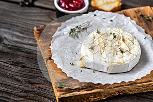 Traditional French homemade baked Camembert cheese with thyme and baguette bread on wooden table