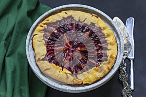 Traditional french pie galette made of corn dough with plum filling on a concrete tray.