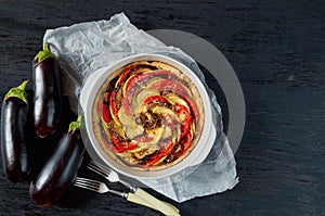 Traditional French pie quiche with eggplants and tomatoes in the baking dish. Homemade eggplant tart on the black background