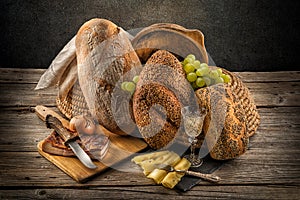 Traditional freshly baked bread with seeds, served with slices of cheese, grape and white wine on a wooden background