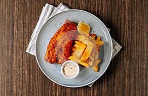 Traditional fried Fish and chips with tartar sauce in white plate on dark wooden background top view