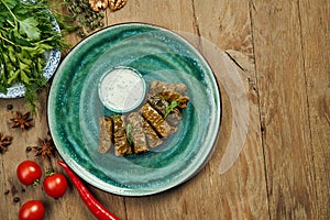 Traditional Georgian dolma - rice with minced meat in grape leaves on a blue plate with yogurt sauce. Wood background. Top view.