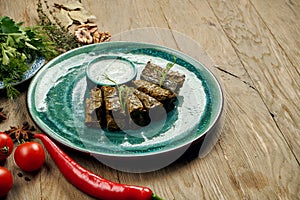 Traditional Georgian dolma - rice with minced meat in grape leaves on a blue plate with yogurt sauce. Wood background. Top view.