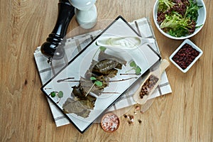 Traditional Georgian dolma - rice with minced meat in grape leaves on a white plate with yogurt sauce. Wood background. Food