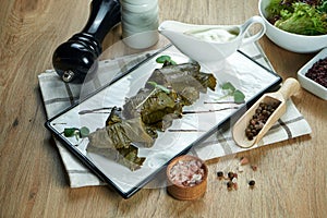 Traditional Georgian dolma - rice with minced meat in grape leaves on a white plate with yogurt sauce. Wood background. Food