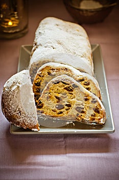 Traditional German Christmas stollen with raisins, nuts, candied fruits, sliced, powdered on plate, festive table setting, lit can