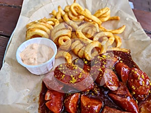 Traditional German currywurst, served with chips on a white plate. Wooden table as background