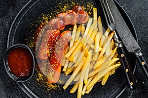 Traditional German currywurst, served with French fries. Black background. Top view