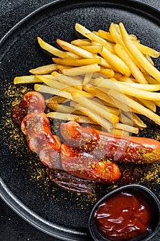 Traditional German currywurst, served with French fries. Black background. Top view