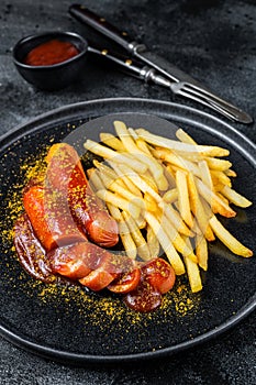 Traditional German currywurst, served with French fries. Black background. Top view