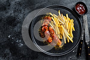 Traditional German currywurst, served with French fries. Black background. Top view. Copy space