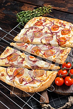 Traditional German pie Flammkuchen or tarte flambee with cream cheese, bacon, tomato and onions. Wooden background. Top
