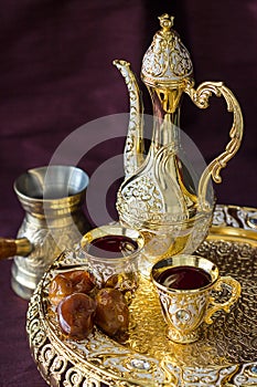 Traditional golden Arabic coffee set with dallah, coffee pot and dates. Dark background.