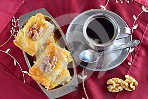 Traditional Greek baklava made with filo dough, sugar syrup and wallnuts on a metal tray with metal coffee cup on a