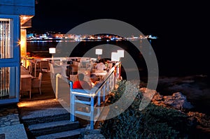 Traditional greek cafe with people wicker furniture on the beach with night views of the Bay and the port of Hersonissos