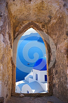 Traditional greek church through an old window in Santorini