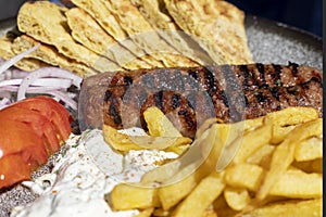 Traditional greek cuisine, grilled kebab with tzatziki dip, fries, pita and additions, dish on a plate in a restaurant, Greece