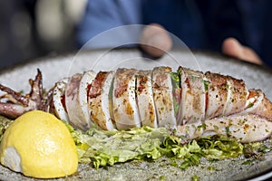 Traditional greek cuisine, grilled squid with piece of lemon and green salad, dish on a plate in a restaurant, Greece
