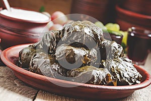 Traditional Greek dolma with meat in grape leaves, yogurt sauce, grapes and red wine on a clay dish, selective focus