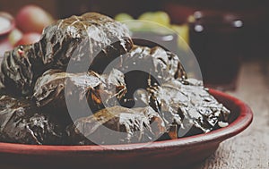 Traditional Greek dolma with meat in grape leaves, yogurt sauce, grapes and red wine on a clay dish, selective focus and toned