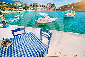 Traditional Greek restaurant with blue and white table and chairs at the sea coast of Assos village. Azure water