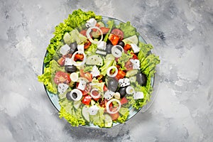 Traditional greek salad with fresh vegetables, feta cheese and olives on concrete background. Top view