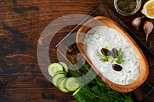 Traditional Greek sauce Tzatziki in olive wooden bowl on old rustic background.