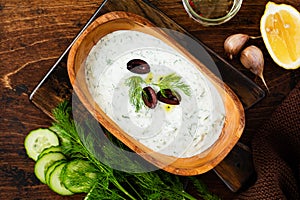 Traditional Greek sauce Tzatziki in olive wooden bowl on old rustic background. Top view
