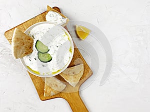 Traditional greek sauce tzatziki in a white bowl on a wooden desk on concrete grey background