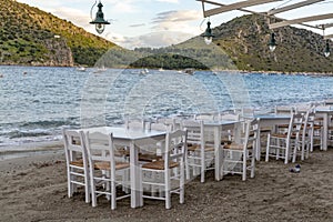 Traditional greek tavern with wooden tables on sandy beach near water waiting for tourists in Tolo, Peloponnese, Greece