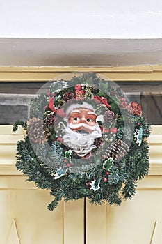 Traditional green and red Christmas crown with face of Santa Claus hung on front door of home