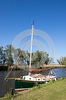 Traditional green wooden sailing boat with mast moored on riverbank