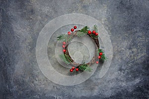 Traditional Handmade Christmas Wreath Green Fir Tree Branches Twigs Holly Berries on Grungy Dark Stone Background. Top View