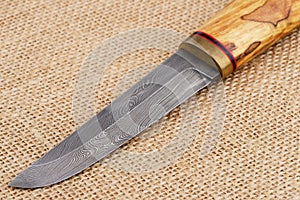 Traditional handmade Finnish knife with the abstract wave pattern of damascus steel and wooden handle over an old sack background.