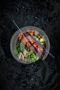 Traditional Hawaiian Poke bowl salad with vegetables and raw salmon fish, top view