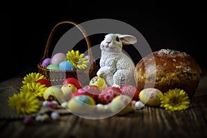 Traditional holiday composition. Hand painting Easter eggs with orthodox sweet bread on a dark wooden table. With rabbit figure.