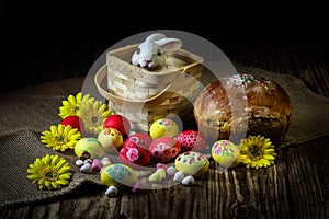 Traditional holiday composition. Hand painting Easter eggs with orthodox sweet bread on a dark wooden table. With rabbit figure.