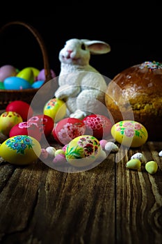 Traditional holiday composition. Hand painting Easter eggs with orthodox sweet bread on a dark wooden table. With rabbit figure.