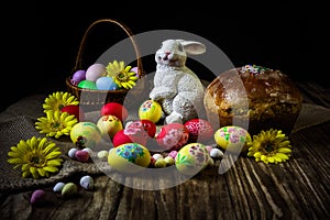 Traditional holiday composition. Hand painting Easter eggs with orthodox sweet bread on a dark wooden table. With rabbit figure.